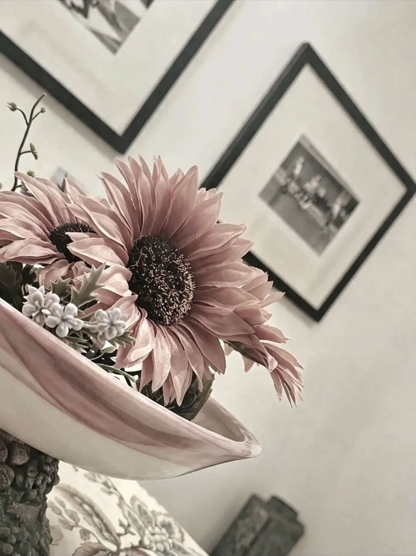 Flor grande de tom rosado em um vaso de cerâmica claro, com quadros emoldurados na parede ao fundo.
